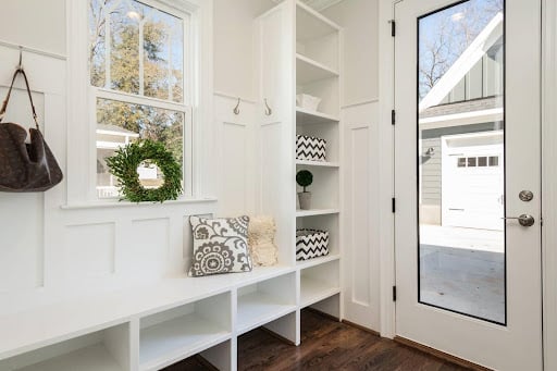 A cozy mudroom house addition with white shelving for shoes, pursues, coats, and more